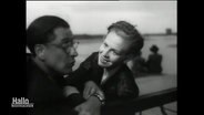 Hildegard Knef sitzt im Film "Film ohne Titel" auf einer Bank neben einem Schauspielkollegen und lächelt diesen ermunternd an. © Screenshot 