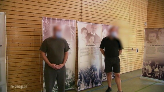 Zwei Männer, deren Gesichter verpixelt sind, stehen vor Ausstellungswänden. © Screenshot 