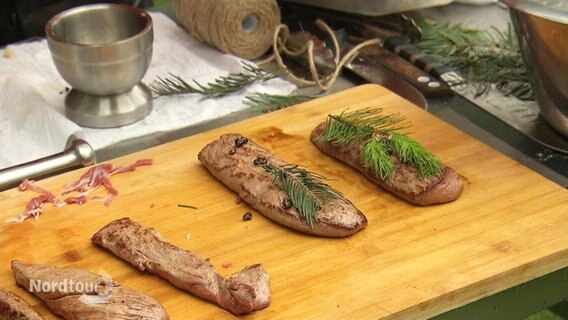 Zwei gegrillte Fleischstücke, auf denen Tannenzweige liegen. © Screenshot 