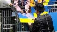 Johannes Oerding gibt ein Autogramm auf einer ukrainischen Flagge. © Screenshot 