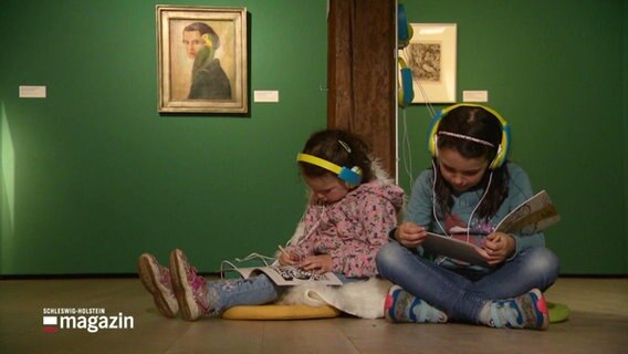 Zwei Mädchen sitzen mit Kopfhörern in einer Ausstellung im Schloss Gottorf. © Screenshot 