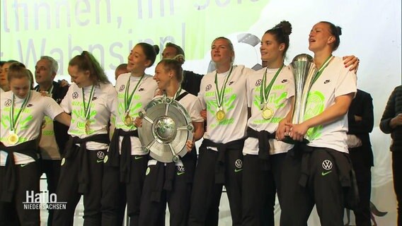 Die Damen vom VfL-Wolfsburg stehen mit einem Pokal auf der Bühne. © Screenshot 
