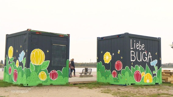 Zwei mit Blumen bemalte Container im Freien, auf einem steht in Druckschrift: "Liebe BUGA". © Screenshot 