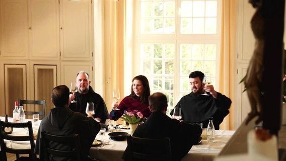 Mehrere Menschen sitzen an einer Tafel und stoßen an. © Screenshot 