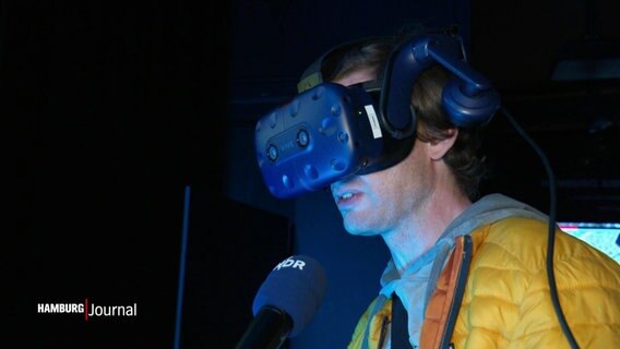 Ein Mann mit großer Virtual Reality Brille spricht in eine Mikrofon. © Screenshot 