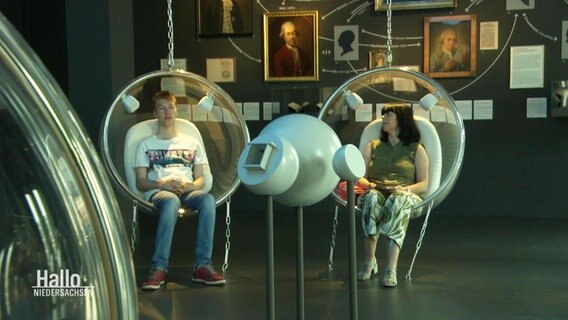 Zwei Ausstellungsbesucher sitzen in kugelförmigen Sesseln. © Screenshot 