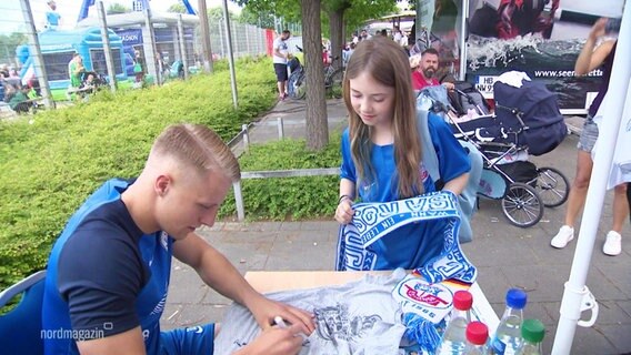 Ein Kind bekommt ein Autogramm von einem Fußballer des Hansa Rostock. © Screenshot 