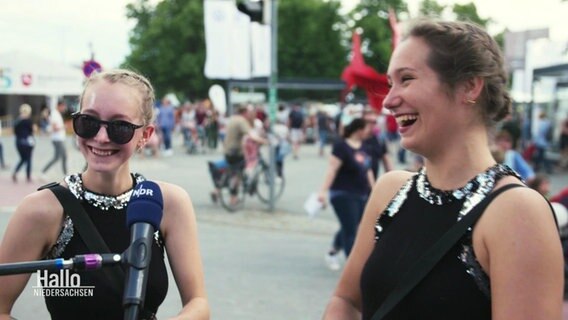 Zwei Frauen geben ein Interview und lachen. Hinter ihnen laufen Menschen auf der Eventmeile im Hannoveraner Maschpark zum "Tag der Niedersachsen". © Screenshot 