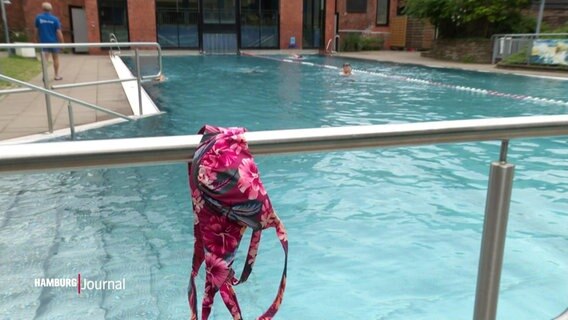 Ein Bikini-Oberteil hängt an einem Handlauf in einem Schwimmbad. © Screenshot 