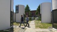 Menschen gehen zwischen Mini-Häusern aus Betonröhren © Screenshot 