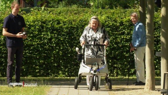 Eine Seniorin schiebt einen Rollator, in den der "digitale Blindenhund" eingebaut ist, durch einen Park. © Screenshot 