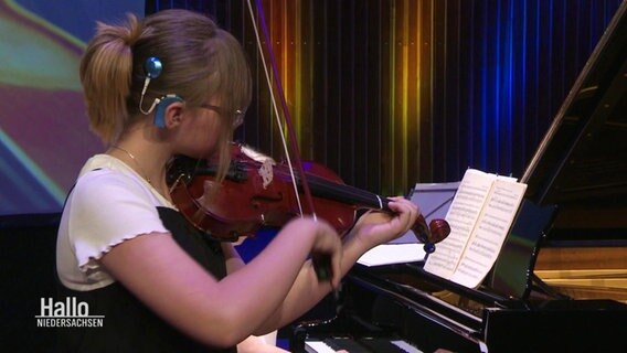Ein Mädchen mit Cochlea-Implantat spielt Geige bei einem Konzert. © Screenshot 