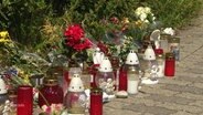 Am Rande eines Gehwegs sind mehrere Grabkerzen und Blumen aufgestellt. © Screenshot 