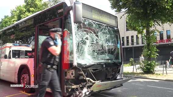 Ein Polizist geht an einem Bus vorbei, dessen Frontscheibe bei einem Unfall stark beschädigt wurde. © Screenshot 