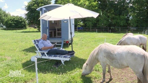 Ein Mann sitzt vor seinem Strandwagen an einer Pferdekoppel. © Screenshot 