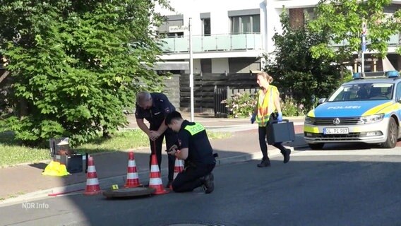 Polizeibeamte untersuchen einen Gullydeckel an einer Straße. © Screenshot 