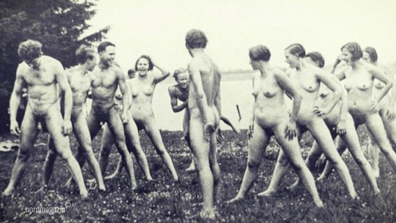 Mehrere Frau und Männer stehen in besonderer Aufstellung nackt am Ufer eines Sees. © Screenshot 