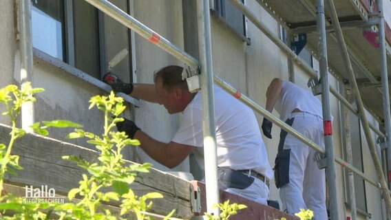 Auf einem Baugerüst streichen mehrere Maler eine Häuserfassade. © Screenshot 