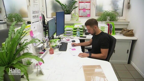 Ein Mann sitzt in seinem gut begrünten Büro am Schreibtisch. © Screenshot 