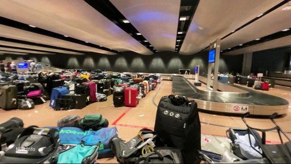 Mehrere Koffer stapeln sich an der Gepäckausgabe eines Flughafens. © Screenshot 