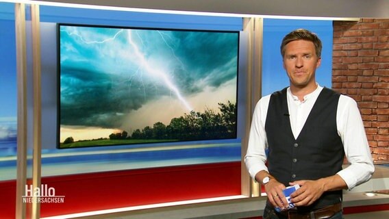 Moderator Arne-Torben Voigts berichtet bei Hallo Niedersachsen von den Folgen der Unwetternacht. Im Hintergrund ist ein Foto eines Blitzeinschlags zu sehen. © Screenshot 