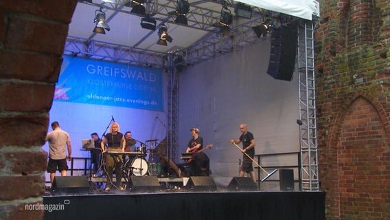 Mehrere Jazz-Musiker stehen bei strömendem Regen auf einer überwchten Bühne. © Screenshot 