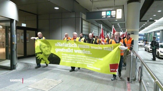 Streikendes Personal hält einen Banner am Hamburger Flughafen. © Screenshot 