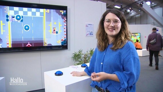 Eine junge Frau steht an einem Messestand, im Hintergrund eine digitale Projektion. © Screenshot 