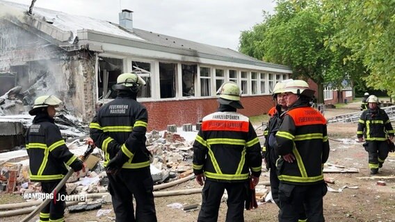 Feuerwehrleute stehen vor einem bei einem Brand beschädigten Gebäude der Stadtteilschule in Hamburg-Finkenwerder. © Screenshot 