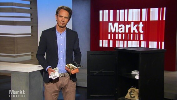 Moderator Jo Hiller im Studio, in den Händen hält er ein Geldscheinbünden und eine Schmuckschatulle. © Screenshot 