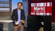Moderator Jo Hiller im Studio, in den Händen hält er ein Geldscheinbünden und eine Schmuckschatulle. © Screenshot 