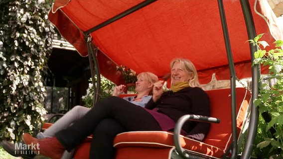 Zwei Frauen sitzen in einer rot gepolsterten Hollywoodschaukel und essen Eis. © Screenshot 