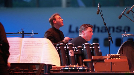 Dirigent Gabriel Venzago und Schlagzeuger Martin Grubinger vor einem Lufthansa-Flugzeug © Screenshot 