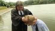 Ein Junge wird von einer Pastorin in einem See getauft © Screenshot 