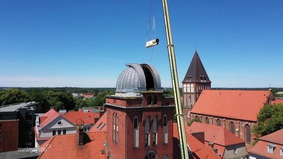 Ein großer Kran hebt ein Teilstück des Teleskops durch die geöffnete Kuppel der Greifswalder Sternwarte. © Screenshot 