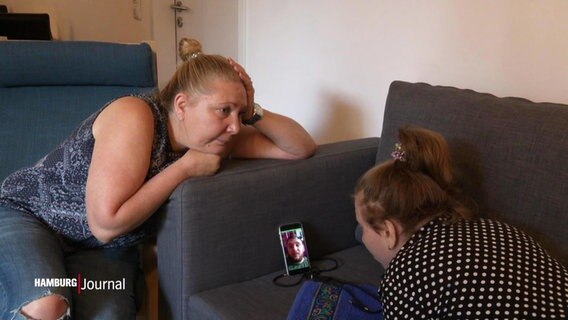 Zwei Frauen chatten auf dem Sofa mit einem Mann übers Handy. © Screenshot 