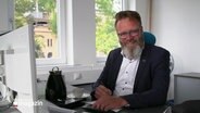 Wirtschaftsminister Claus Ruhe Madsen sitzt freundlich lächelnd an einem Schreibtisch. © Screenshot 