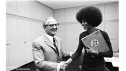 Die Amerikanische Bürgerrechtlerin Angela Davis schüttelt dem Staatsratsvorsitzenden der DDR, Erich Honecker, in einem Büro die Hand. © Screenshot 