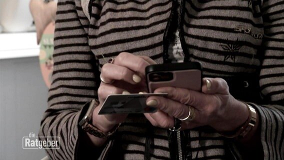 Großaufnahme der Hände einer Frau, die auf einem Smartphone tippt und eine Kreditkarte in der Hand hält. © Screenshot 
