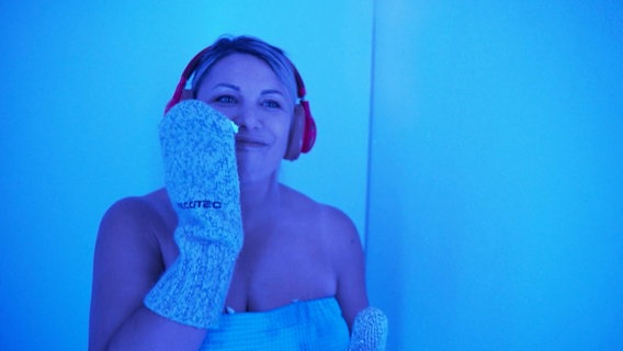 Eine Frau mit Handschuhen und Ohrenschützern in der Kältekammer. © Screenshot 
