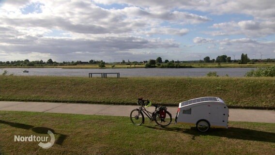 Ein Fahrrad steht mit einem kleinen Anhänger an der Elbe. © Screenshot 