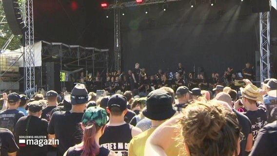 Schwarz gekleidete Metal-Fans vor einer Bühne beim Eröffnungskonzert des Wacken Open Air 2022. © Screenshot 