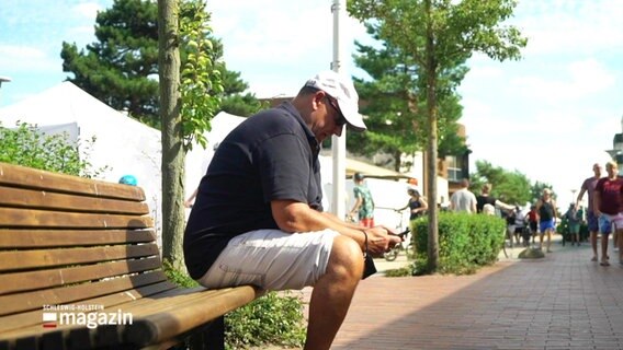 Ein Urlauber auf einer Bank mit seinem Handy. © Screenshot 
