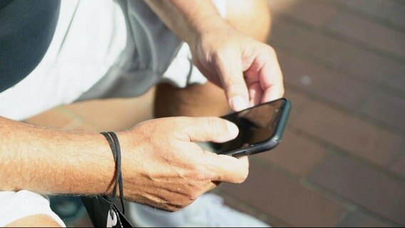 Ein Mann hält ein Handy in der Hand. © Screenshot 