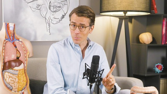 Dr. Wimmer sitzt auf einem Sofa und spricht in ein Mikrofon. © Screenshot 