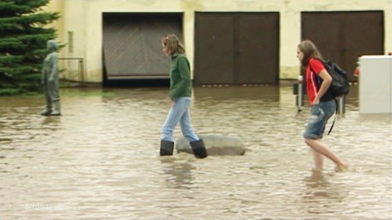Zwei Personen laufen mit Gummistiefeln durch überschwemmtes Gebiet © Screenshot 