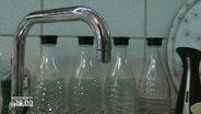 Vier Wasserflaschen vor einem Wasserhahn. © Screenshot 
