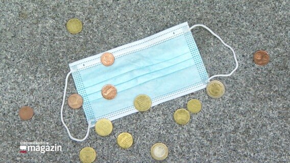 Symbolbild: Einige Cent- und Eurostücke auf einer OP-Maske. © Screenshot 