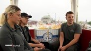 Drei Personen sitzen in der Gondel des Riesenrads auf dem Hamburger Dom. © Screenshot 