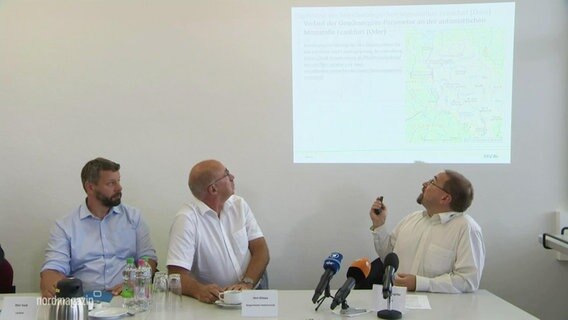 Bei einer Pressekonferenz blicken mehrere Männer auf eine Wand projizierte Karte der Oder. © Screenshot 